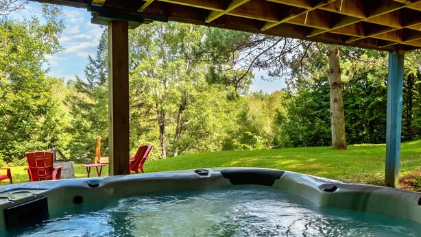 Una banyera d'hidromassatge sota una pérgola de fusta, amb un jardí verdós i arbres al fons.