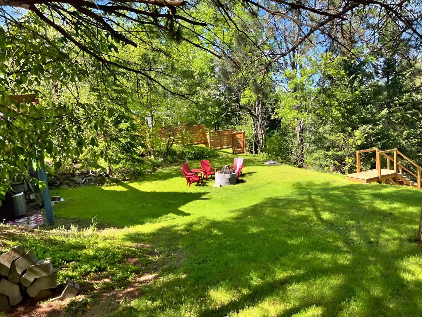 Un jardin bien entretenu avec une terrasse en bois, des chaises rouges et un foyer extérieur.