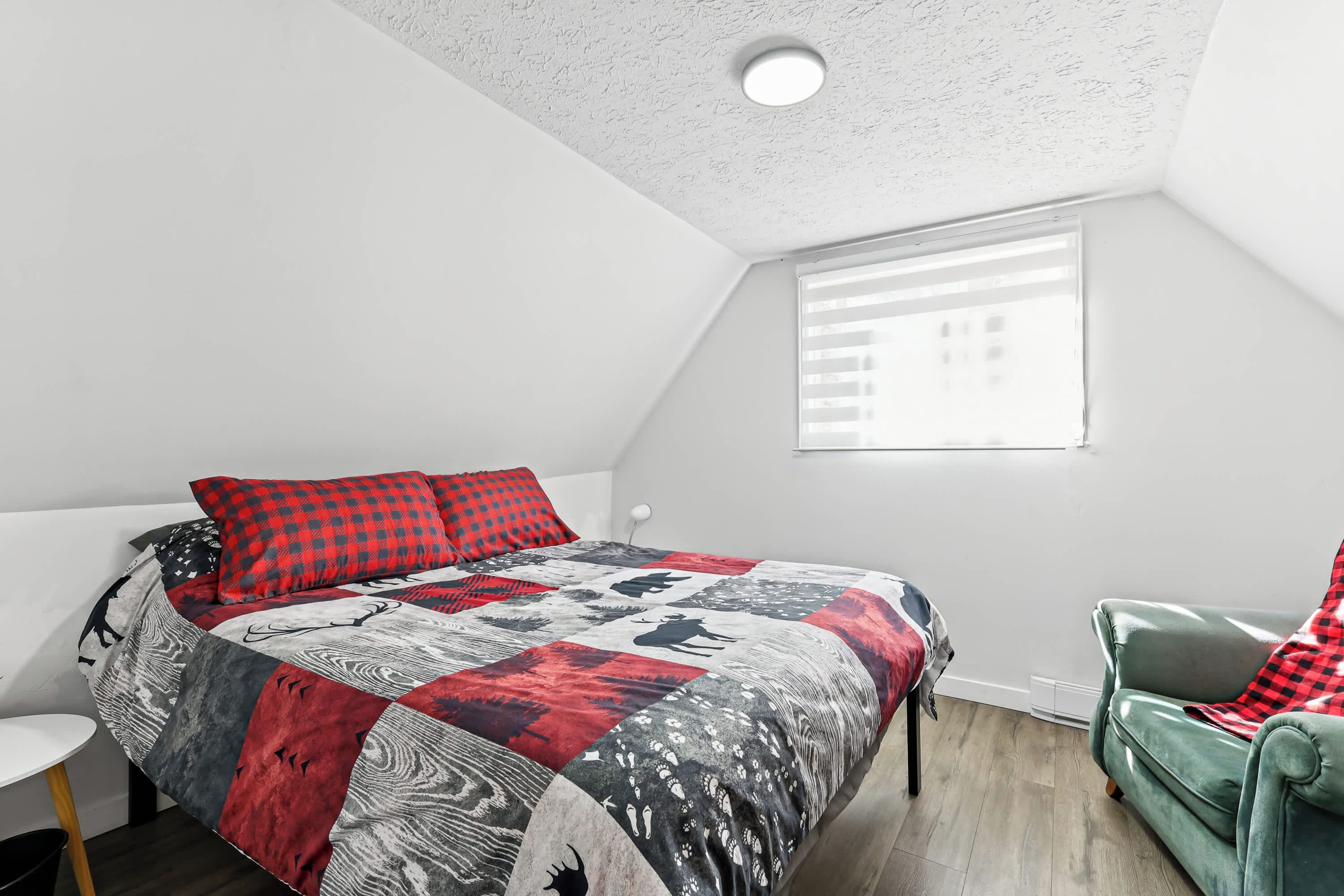A bedroom with a bed, a chair, a window, and a ceiling light.