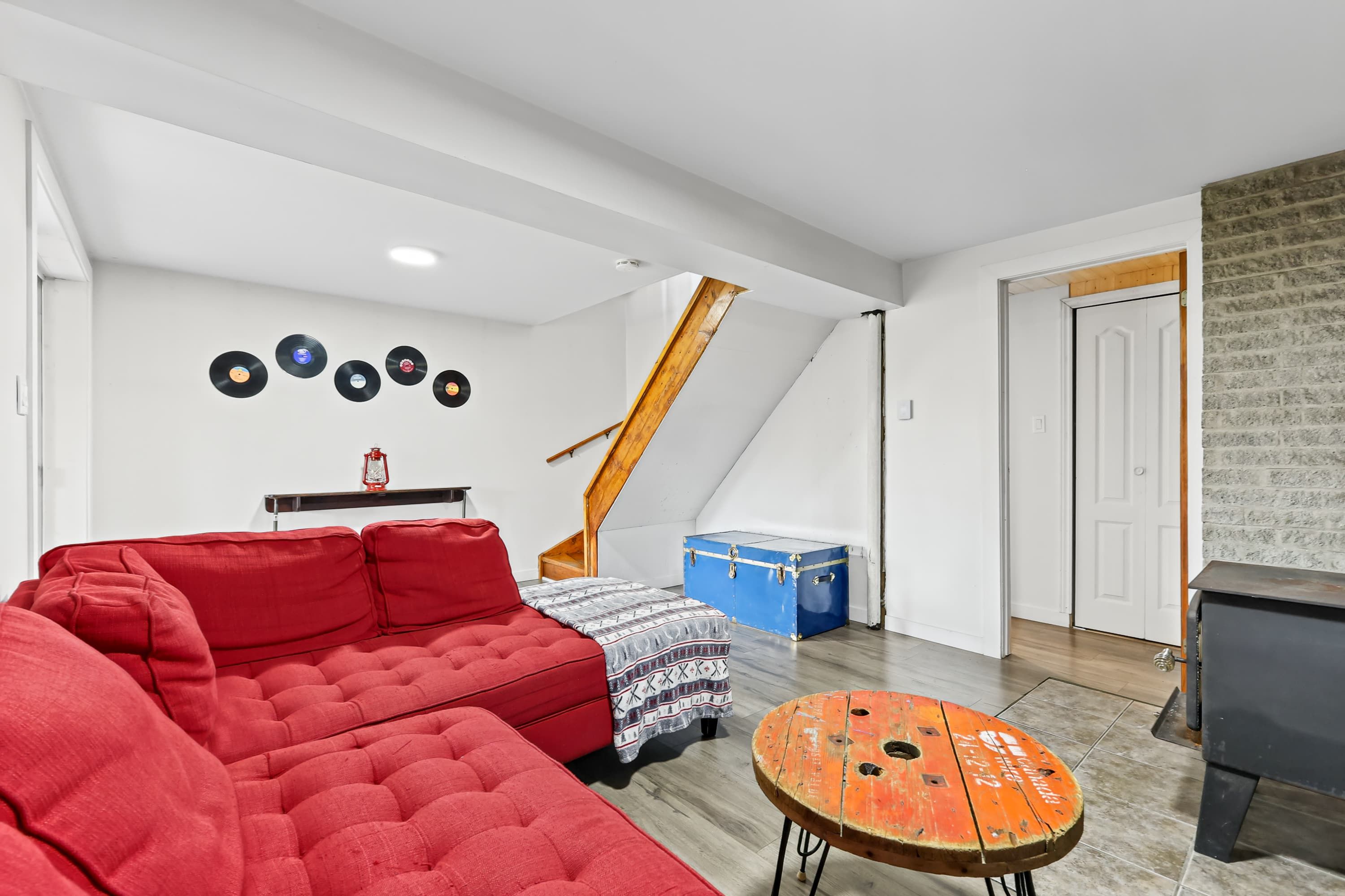 A room with a red sofa, a patterned ottoman, a blue trunk, and a wooden staircase.