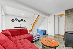 A room with a red sofa, a patterned ottoman, a blue trunk, and a wooden staircase. - Waterfront with Spa | Le Retro (Val-Joli)