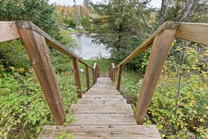 A wooden staircase leading to a bridge over a body of water, surrounded by greenery. - Waterfront with Spa | Le Retro (Val-Joli)