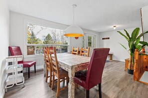 A dining area with a wooden table, red chairs, a white ceiling light, and large windows. - Waterfront with Spa | Le Retro (Val-Joli)