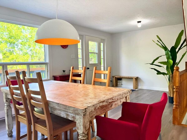 A dining area with a rustic wooden table, wooden chairs, a red upholstered chair, a white pendant light, and a potted plant. - Waterfront with Spa | Le Retro (Val-Joli)