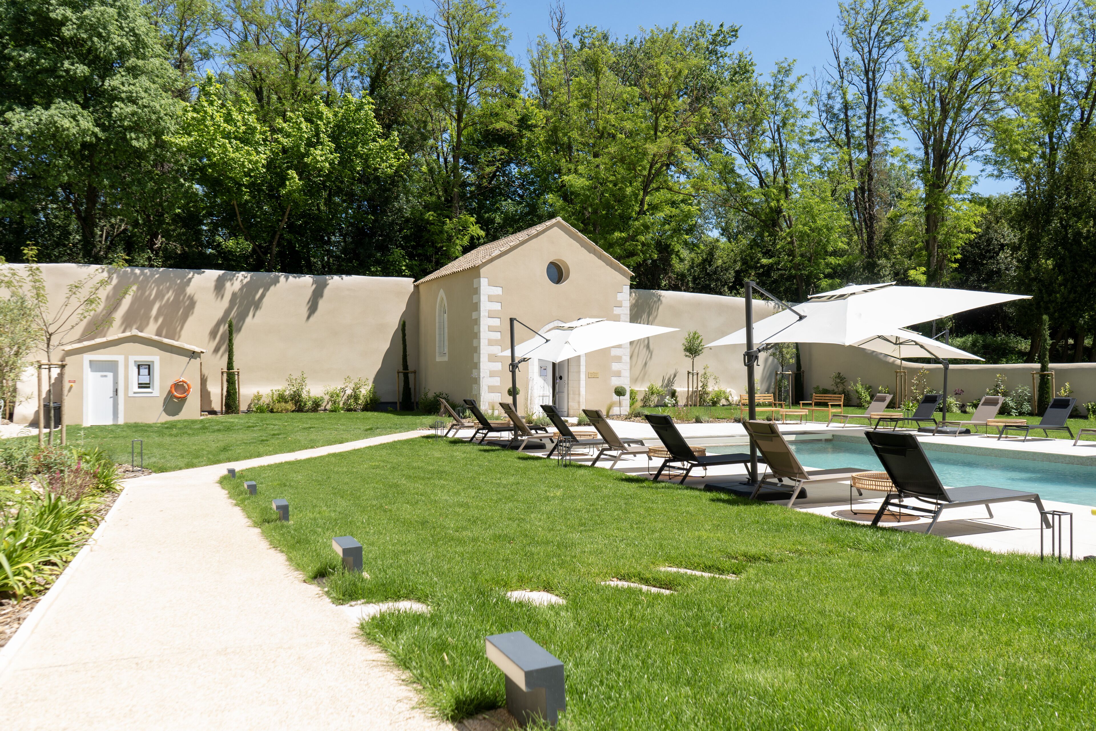A pool area with lounge chairs and umbrellas, surrounded by a well-maintained lawn and trees.