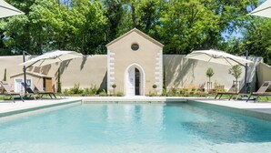 A swimming pool with lounge chairs and umbrellas, surrounded by a beige wall and trees. - Château de L'Insolas (Villeneuve-lès-Avignon)