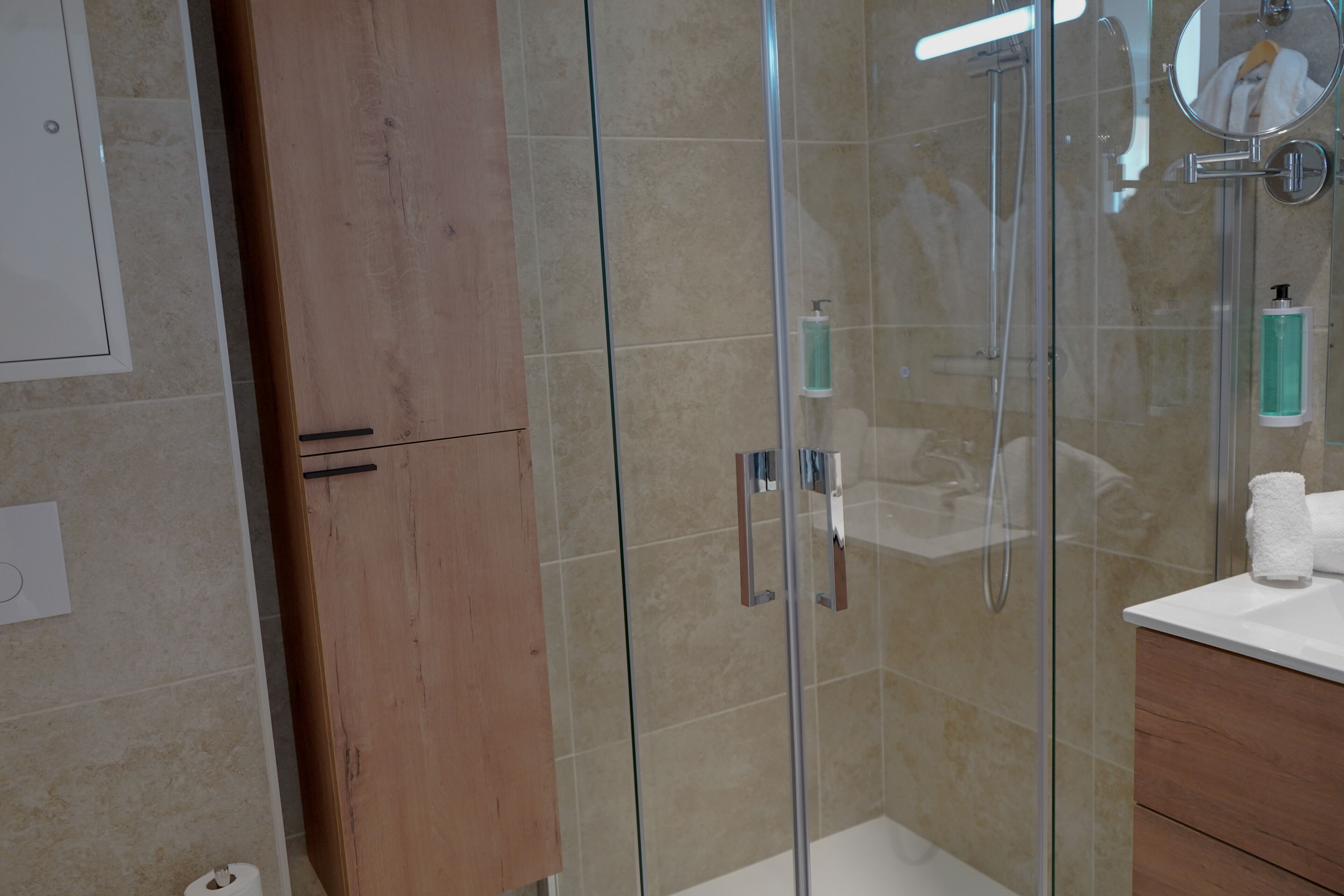 A modern bathroom with a glass-enclosed shower, wooden cabinets, and a white countertop.