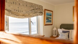 Ein Schlafzimmer mit Meerblick, ein Bett mit Kissen, ein Nachttisch und ein gerahmtes Bild an der Wand.