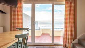 Ein Zimmer mit einem Holztisch, grünen gepolsterten Stühlen und einer Schiebetür, die auf einen Balkon mit Meerblick führt.