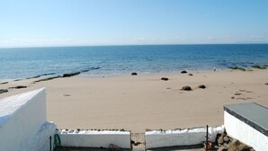 Ein Strand mit freiem Blick auf das Meer, sandigem Ufer und einigen Felsen.