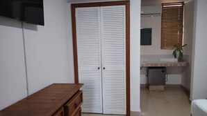 Un dormitorio con un aparador de madera, un armario con puertas correderas, una cama, un escritorio pequeño y una ventana con persianas.