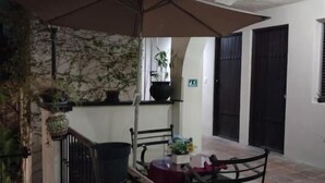 Un patio al aire libre con mesa y sillas, una sombrilla colgante y macetas con plantas.