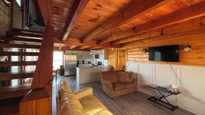 Interior acogedor de una cabaña con techo de madera, un sofá, un televisor y una zona de cocina.