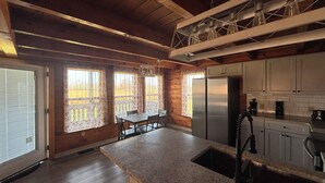Una cocina con vigas de madera, encimera de granito, refrigerador de acero inoxidable y ventana con vistas a árboles.