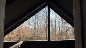 Habitación de madera en el ático con vistas a árboles a través de un ventanal triangular.