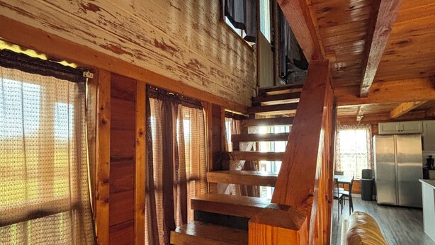 Un interior de madera con una escalera que sube a un nivel superior, un sofá y una zona de cocina.