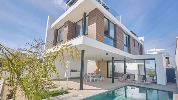 Ein modernes, zweistöckiges Haus mit Swimmingpool, Sitzgelegenheiten im Freien und freiem Blick auf die umliegende Landschaft.