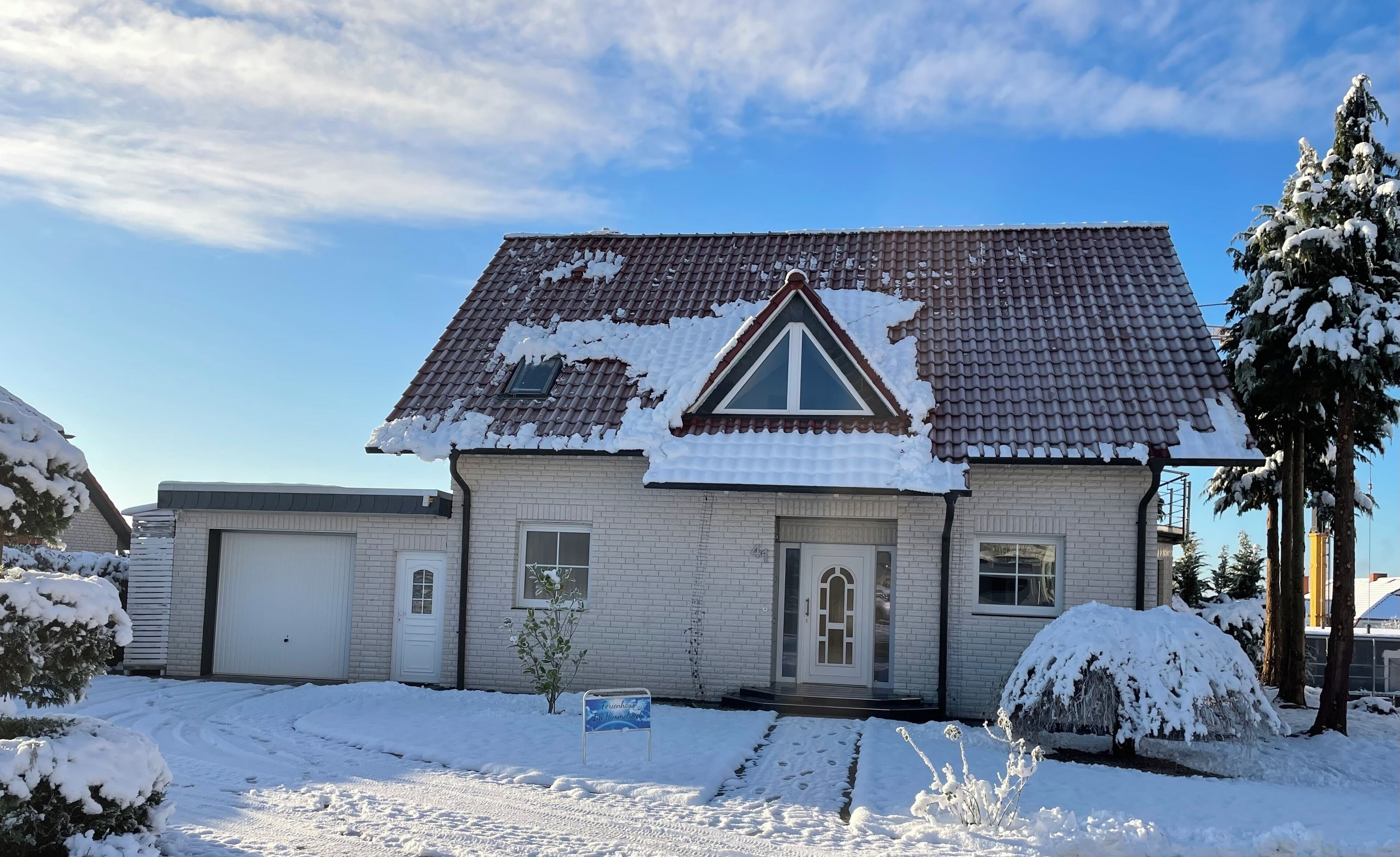 A two-story house with a tiled roof, a front door, and a small garden area with snow.