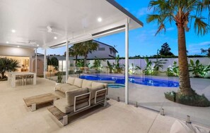 A modern outdoor living area with a pool, a sofa, and a dining table. - Casa Palma in Mermaid Waters (Gold Coast)