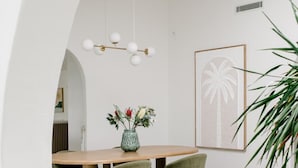 A modern dining area with a round wooden table, green upholstered chairs, a vase with flowers, and a cactus display. - Casa Palma in Mermaid Waters (Gold Coast)