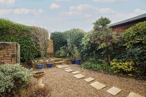 A garden with a gravel path, potted plants, a birdbath, and a wooden fence. - Host Stay Amberleigh (Seahouses)