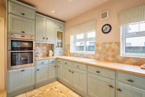 A kitchen with light blue cabinets, two ovens, a sink, and a window with a view. - Host Stay Amberleigh (Seahouses)