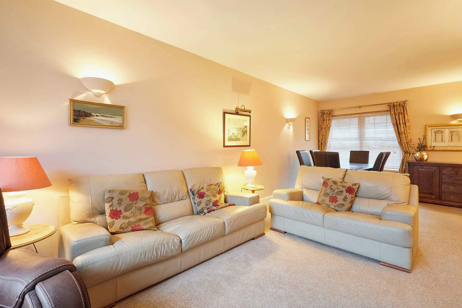 A living room with two sofas, a coffee table, and a lamp. There are framed pictures on the wall and a window with curtains.