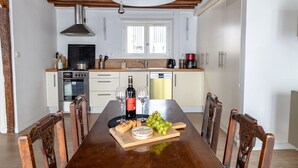 Un comedor con una mesa de madera dispuesta para una comida, una cocina al fondo y un ventanal sobre el fregadero.