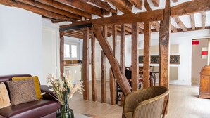 Una sala de estar con vigas de madera a la vista, un sofá de cuero rojo, un sill ón de mimbre y un jarrón con flores secas.