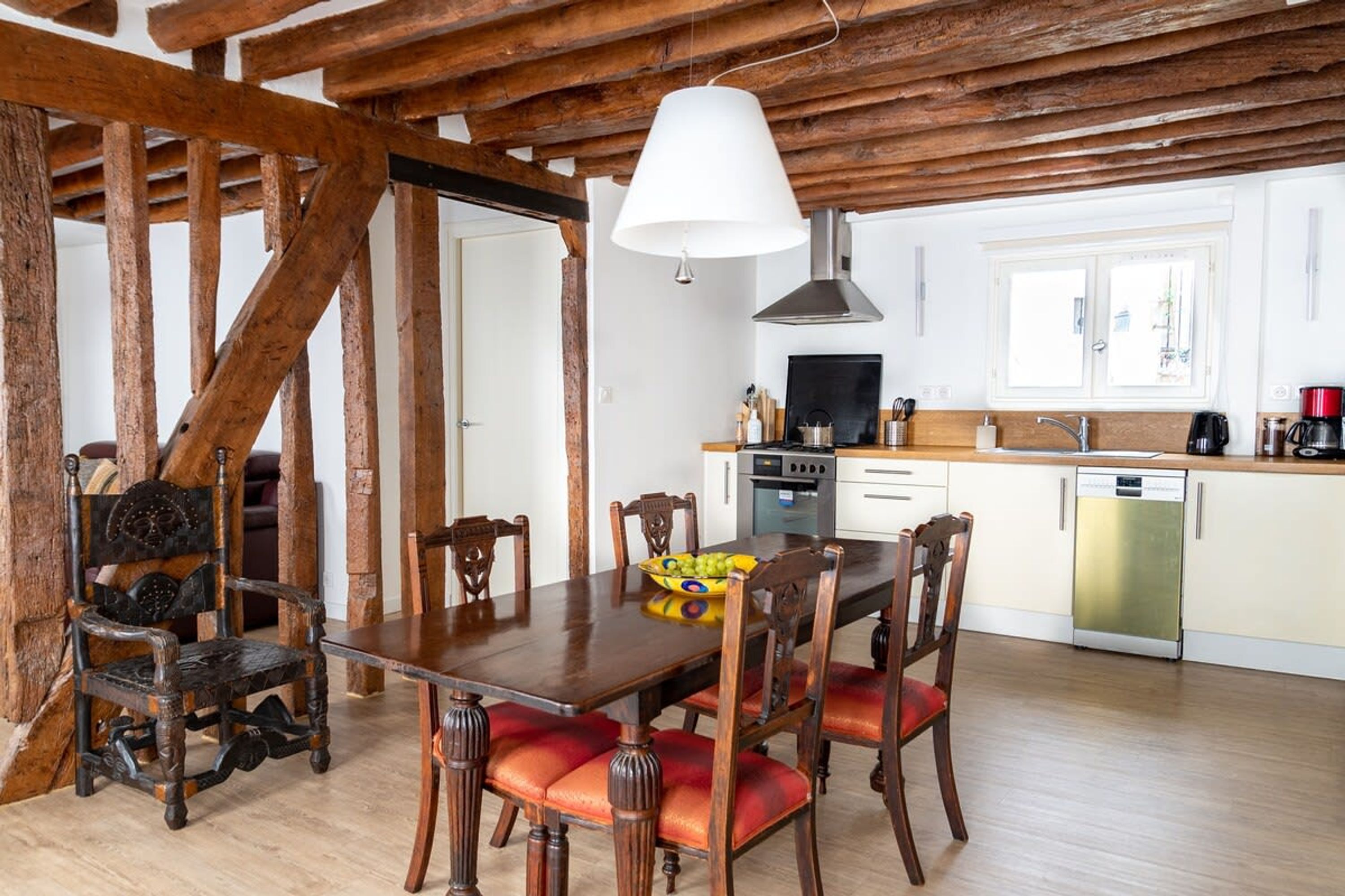 Ein rustikaler Essbereich mit Holztisch und -stühlen, im Hintergrund eine moderne Küche und ein großes Fenster.