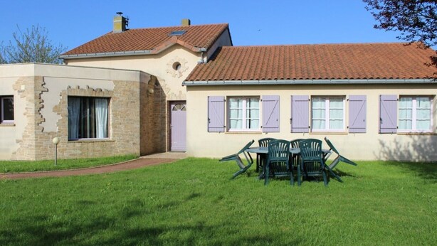 Une maison à deux étages avec une façade en pierre, un toit en tuiles et une pelouse agrémentée de meubles d’extérieur.