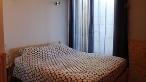 Une chambre à coucher avec un lit, une table de chevet, une lampe fixée au mur et une fenêtre avec des rideaux.