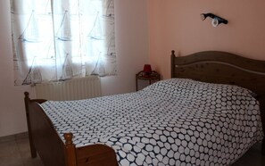 Ein Schlafzimmer mit Bett, Heizkörper, kleinem Tisch und einer Wandleuchte.