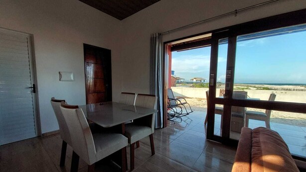 A dining area with a table and chairs, a sofa, and a large sliding glass door leading to a beach view.