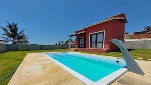 A swimming pool with a tiled deck, a red building with a sloped roof, and a clear blue sky.