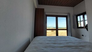 A bedroom with a bed, a window with a view of the beach, and a wooden ceiling.