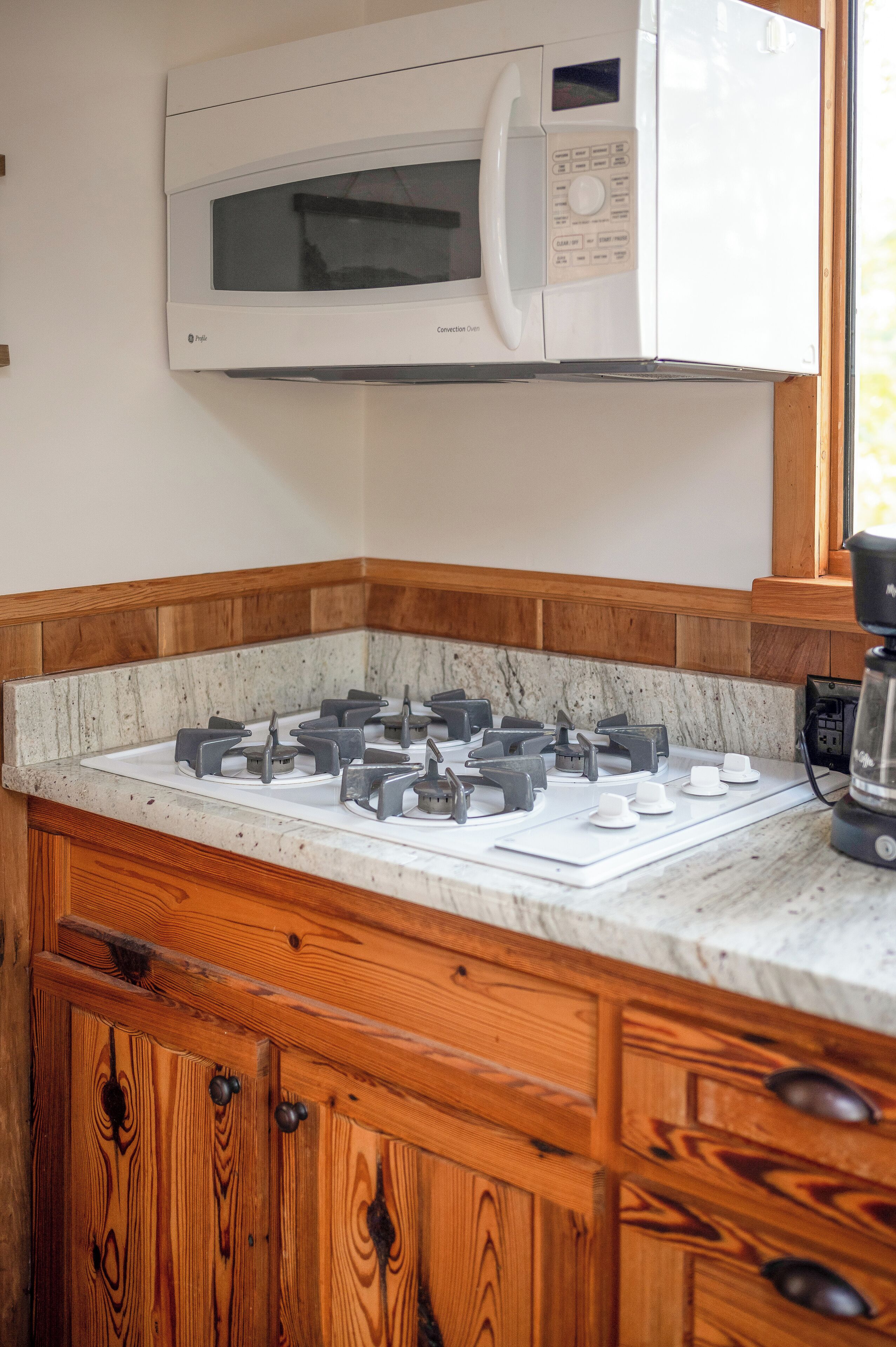 A kitchen with a built-in microwave, gas stove, wooden cabinets, and a marble countertop.