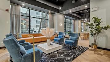 A modern lounge area with a sofa, armchairs, and a coffee table. Large windows offer a view of the street outside.