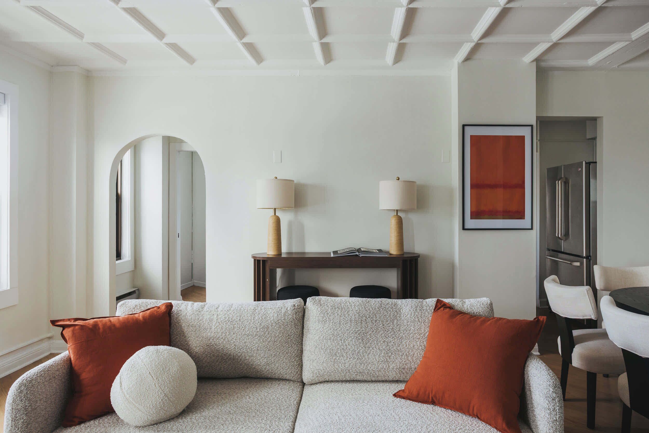 A living room with a sectional sofa, a dining table with chairs, a refrigerator, and a framed artwork on the wall.