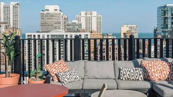 An outdoor seating area with a sofa, chairs, and a table, overlooking a cityscape with high-rise buildings.