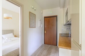 Una habitación de hotel con cama, puerta de madera, kitchenette y un accesorio de luz montado en la pared.