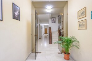 A hallway with a potted plant, framed pictures on the walls, and a staircase in the distance.