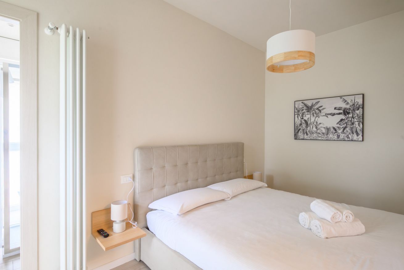 A bedroom with a bed, bedside table, lamp, and a framed picture on the wall.