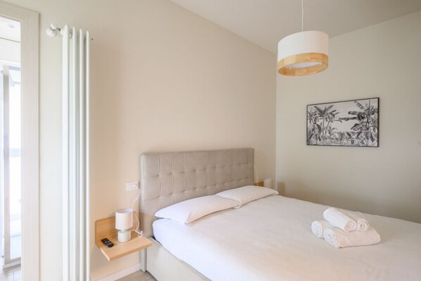 Un dormitorio con cama, mesita de noche, lámpara y un cuadro en la pared.
