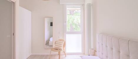 A bedroom with a large bed, a chair, a window with curtains, a mirror, and a ceiling light fixture.