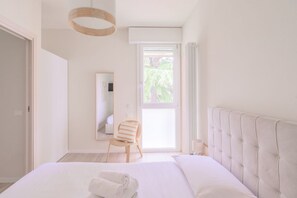 Un dormitorio con una cama grande, una silla, una ventana con cortinas, un espejo y una lámpara en el techo.