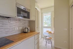 Una cocina moderna con horno empotrado, cafetera y ventana con vistas a un balcón.