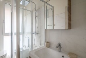 Un baño moderno con cabina de ducha de vidrio, un lavabo blanco y un espejo sobre el lavabo.