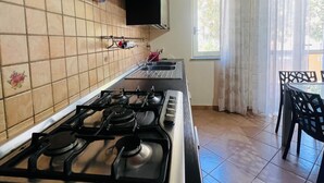Una cocina con estufa a gas, extractor de humos y una ventana con cortinas.