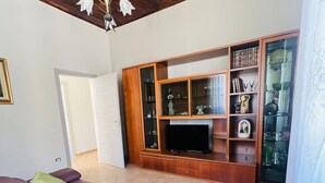 Una sala de estar con un sofá morado, un mueble de entretenimiento de madera con puertas de vidrio y un ventilador de techo.